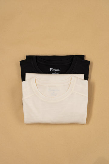 The off white and black merino wool longsleeve tees are neatly folded on a sand background.