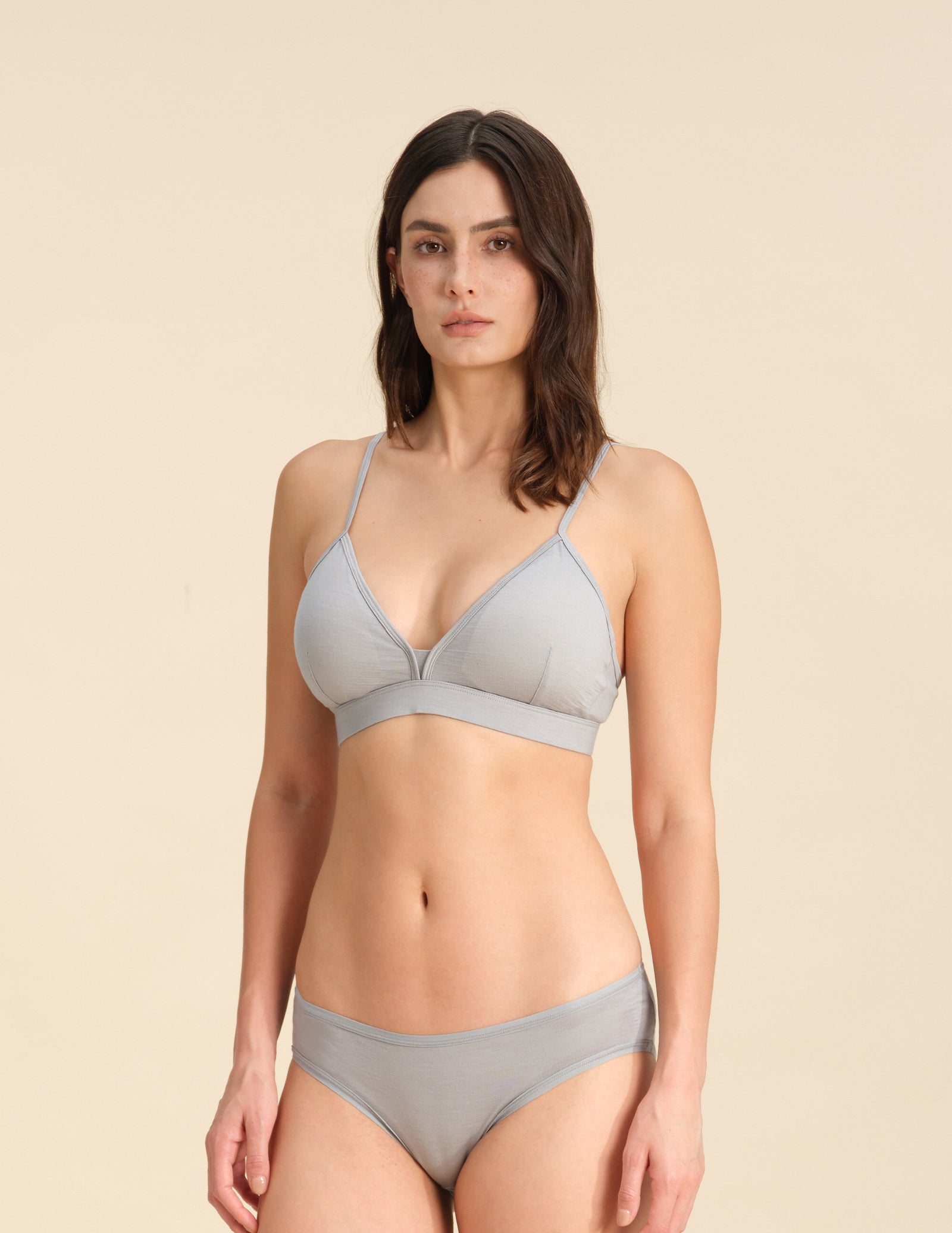 Woman wearing a grey triangle bra and bikini set against a sand background
