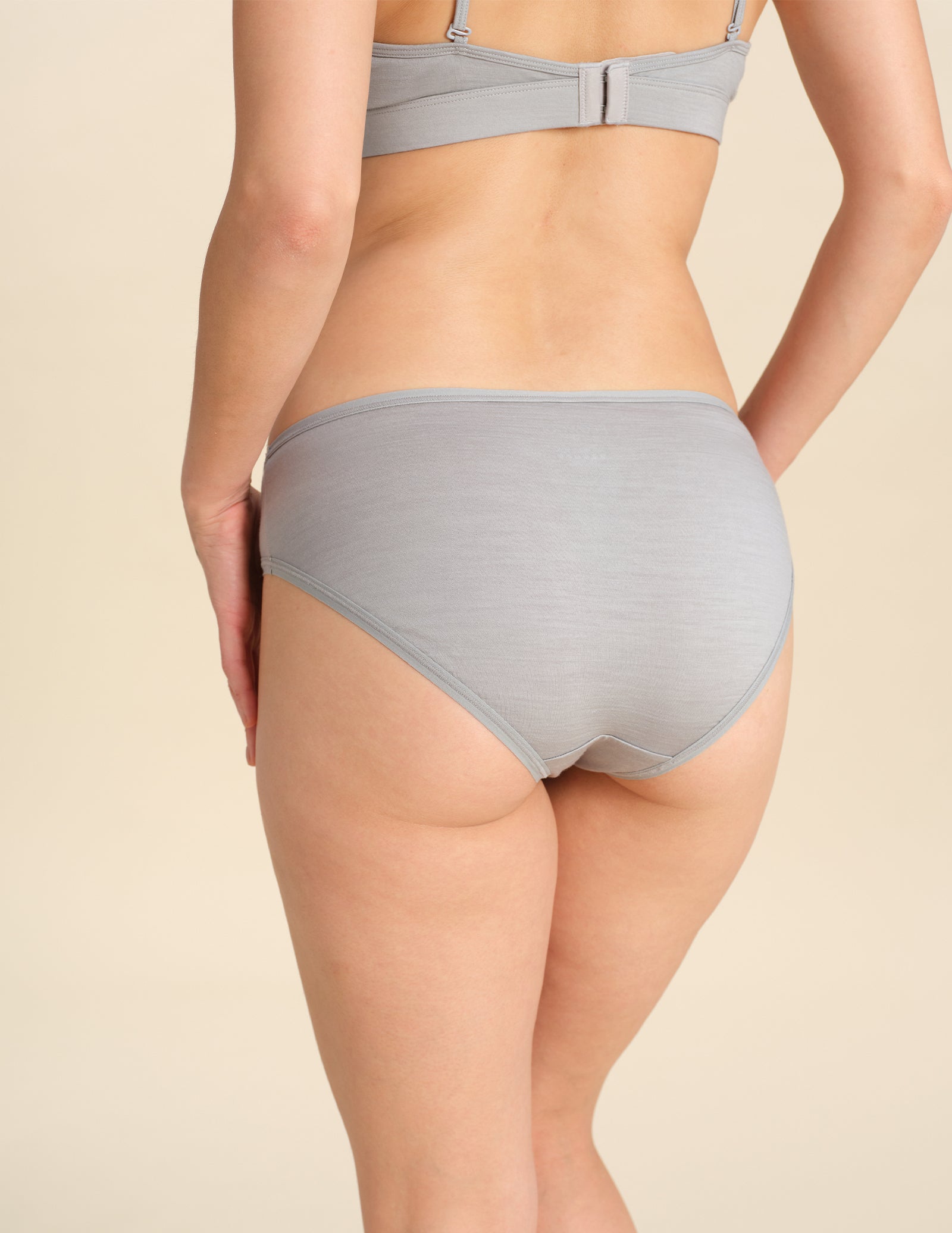 Back view of person wearing grey bikini brief against a neutral background