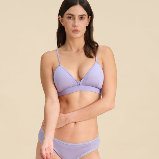 Woman wearing a lavender triangle bra and bikini set against a sand background