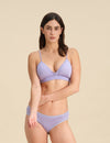 Woman wearing a lavender triangle bra and bikini set against a sand background