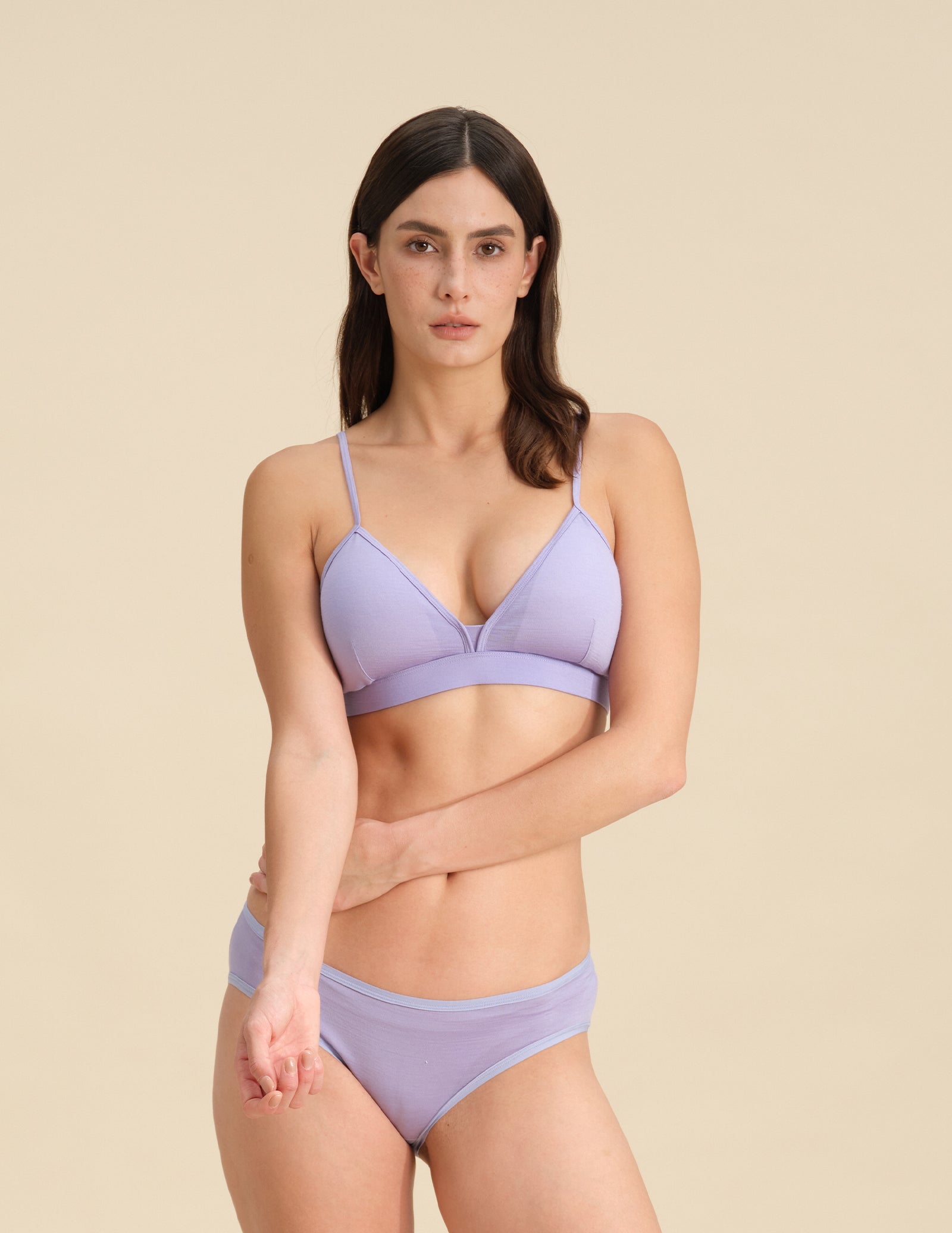 Woman wearing a lavender triangle bra and bikini set against a sand background