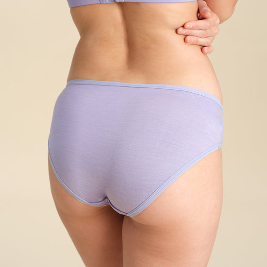 Back view of person wearing a lavender bikini brief against a sand background