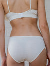 Person wearing off white bra and underwear set against a neutral background