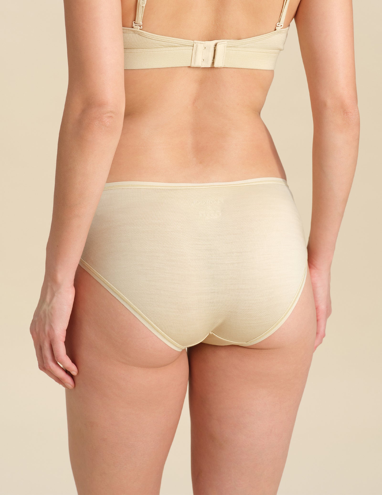 Back view of person wearing sand bikini brief against a neutral background.