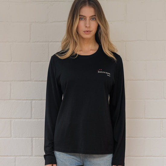 Person wearing a black long-sleeve shirt with a logo against a light brick wall.