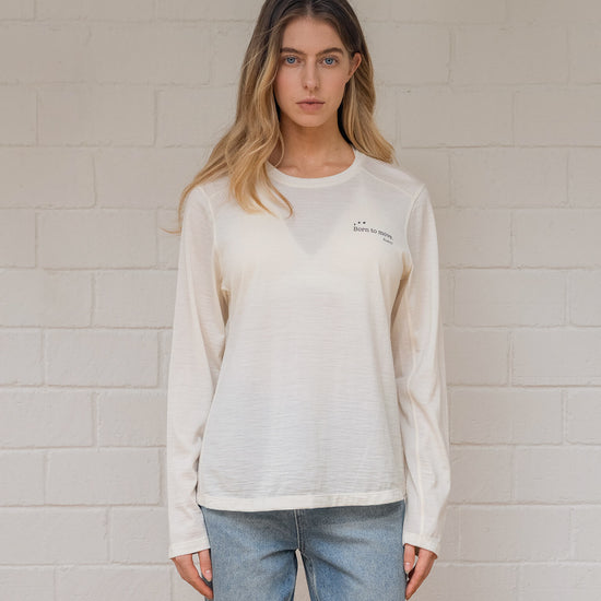 Woman wearing off  white sweatshirt with a logo against a light brick wall
