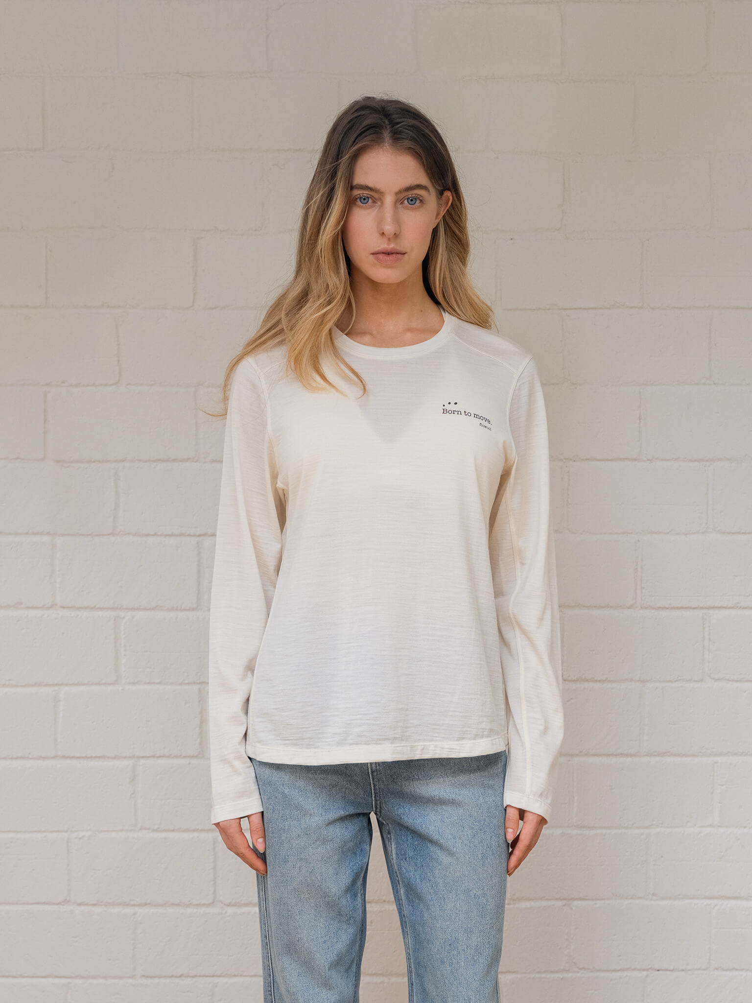 Woman wearing off  white sweatshirt with a logo against a light brick wall