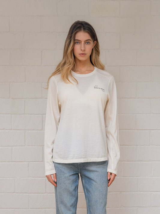 Woman wearing off  white sweatshirt with a logo against a light brick wall