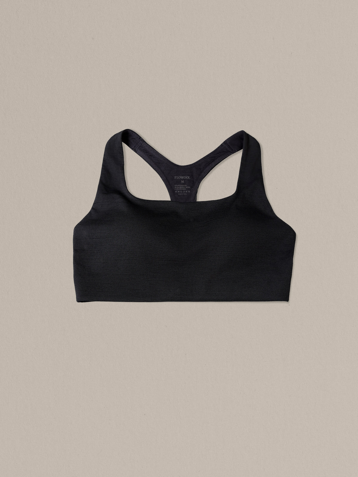Women's black merino wool sports bra on a neutral sand background.