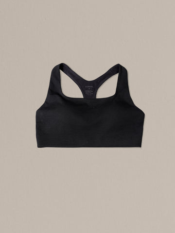 Women's black merino wool sports bra on a neutral sand background.
