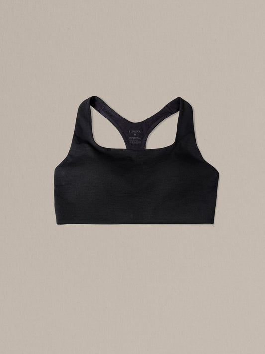 Women's black merino wool sports bra on a neutral sand background.