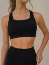 Close-up of a woman wearing a merino sports bra top against the white wall.
