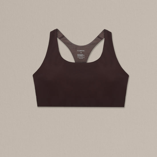 Women's chocolate merino wool sports bra on a neutral sand background.