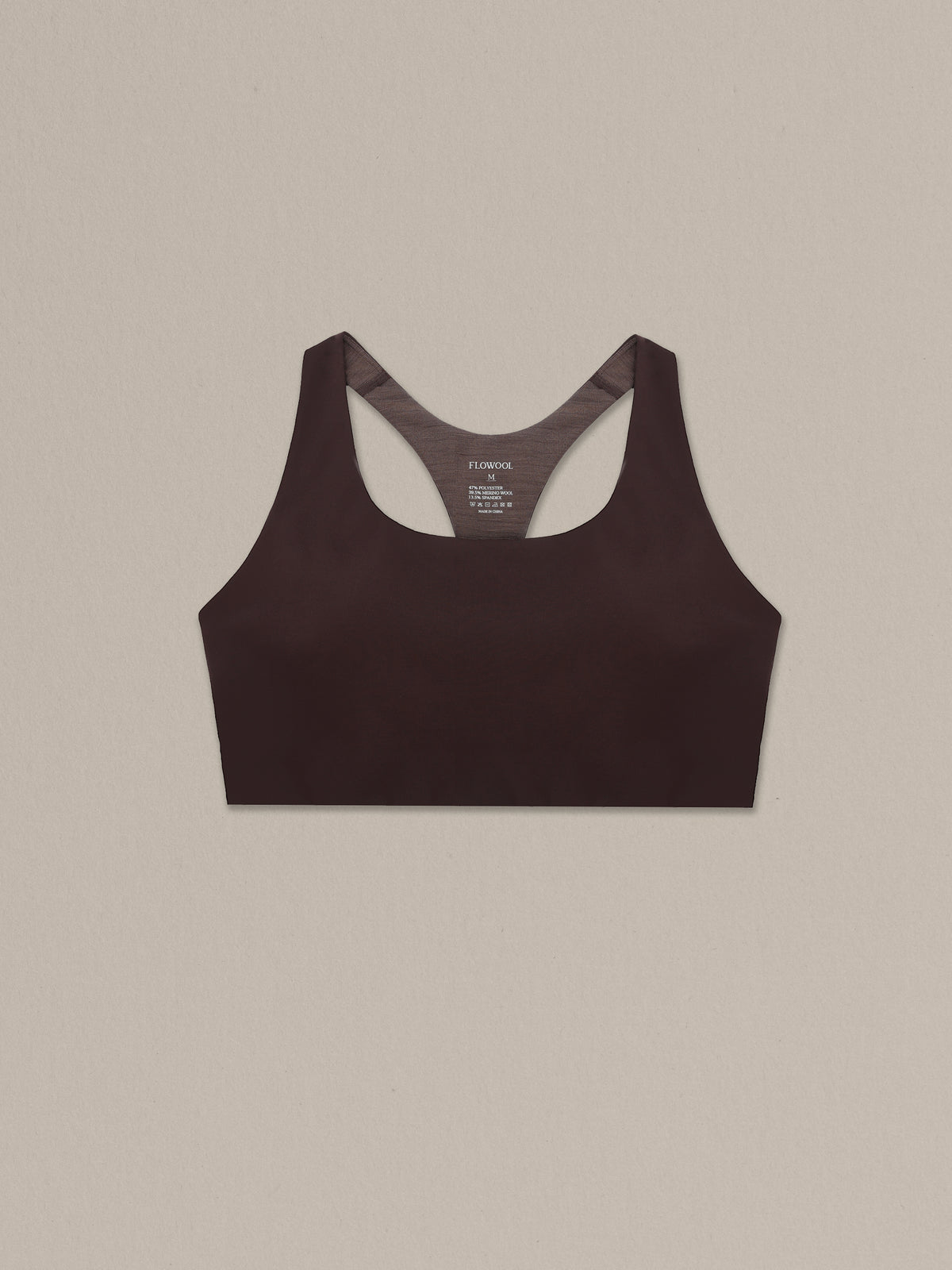 Women's chocolate merino wool sports bra on a neutral sand background.