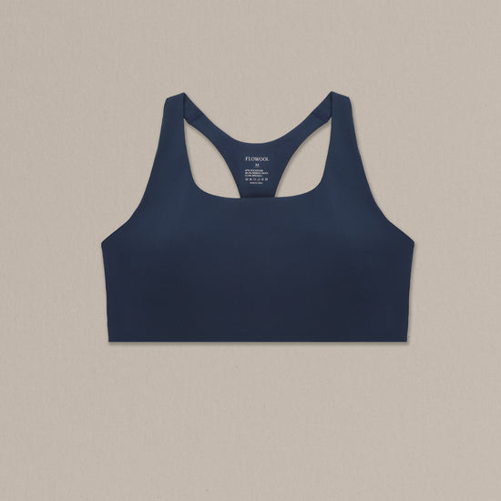 Women's navy merino wool sports bra on a neutral sand background.