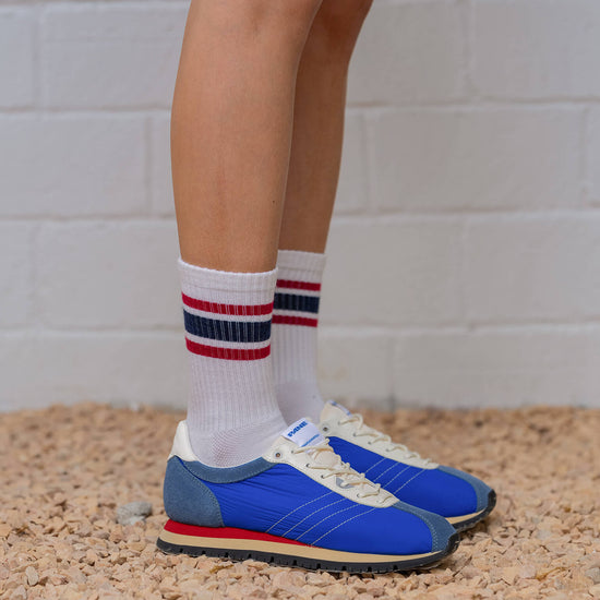 Blue running shoes with white socks featuring red and blue stripes on a textured surface.