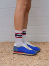 Blue running shoes with white socks featuring red and blue stripes on a textured surface.