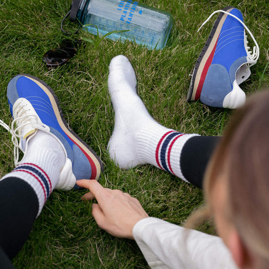 Two pairs of feet wearing colorful sneakers on grass with a water bottle nearby.
