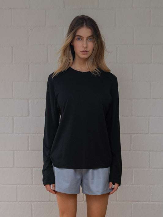 Person wearing a black long-sleeve shirt and light blue shorts against a white brick wall.