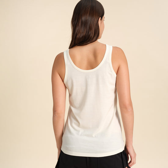 Back view of a woman wearing a white Merino wool scoop tanks against a sand background.