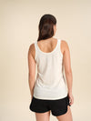 Back view of a woman wearing a white Merino wool scoop tanks against a sand background.