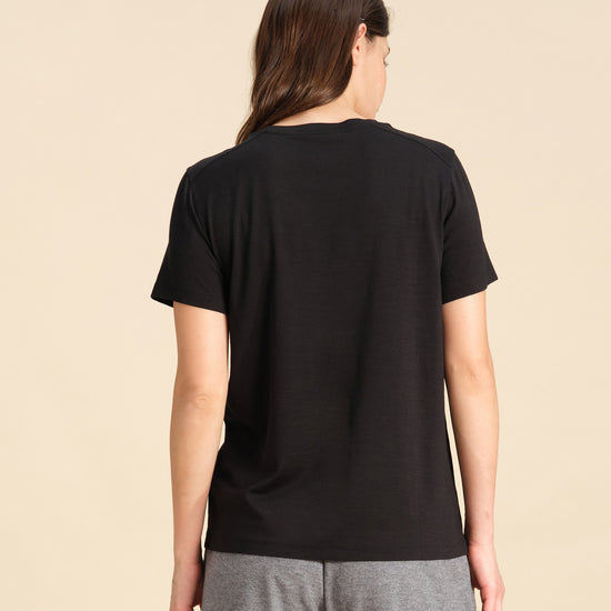 Back view of a woman wearing a black Merino wool t-shirt against a sand background.