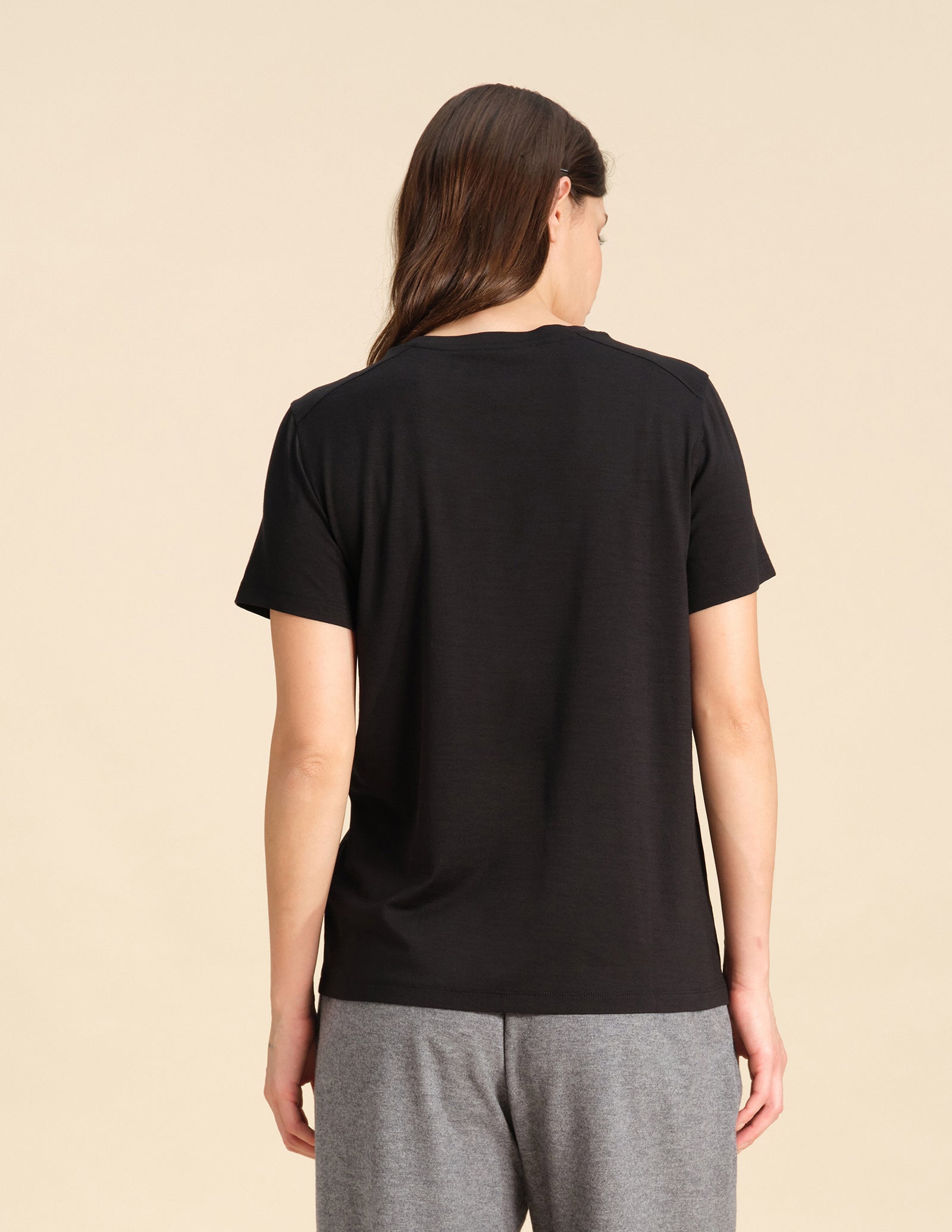 Back view of a woman wearing a black Merino wool t-shirt against a sand background.
