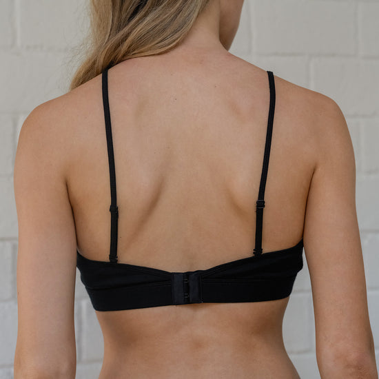 Person wearing a black bra against a white brick wall