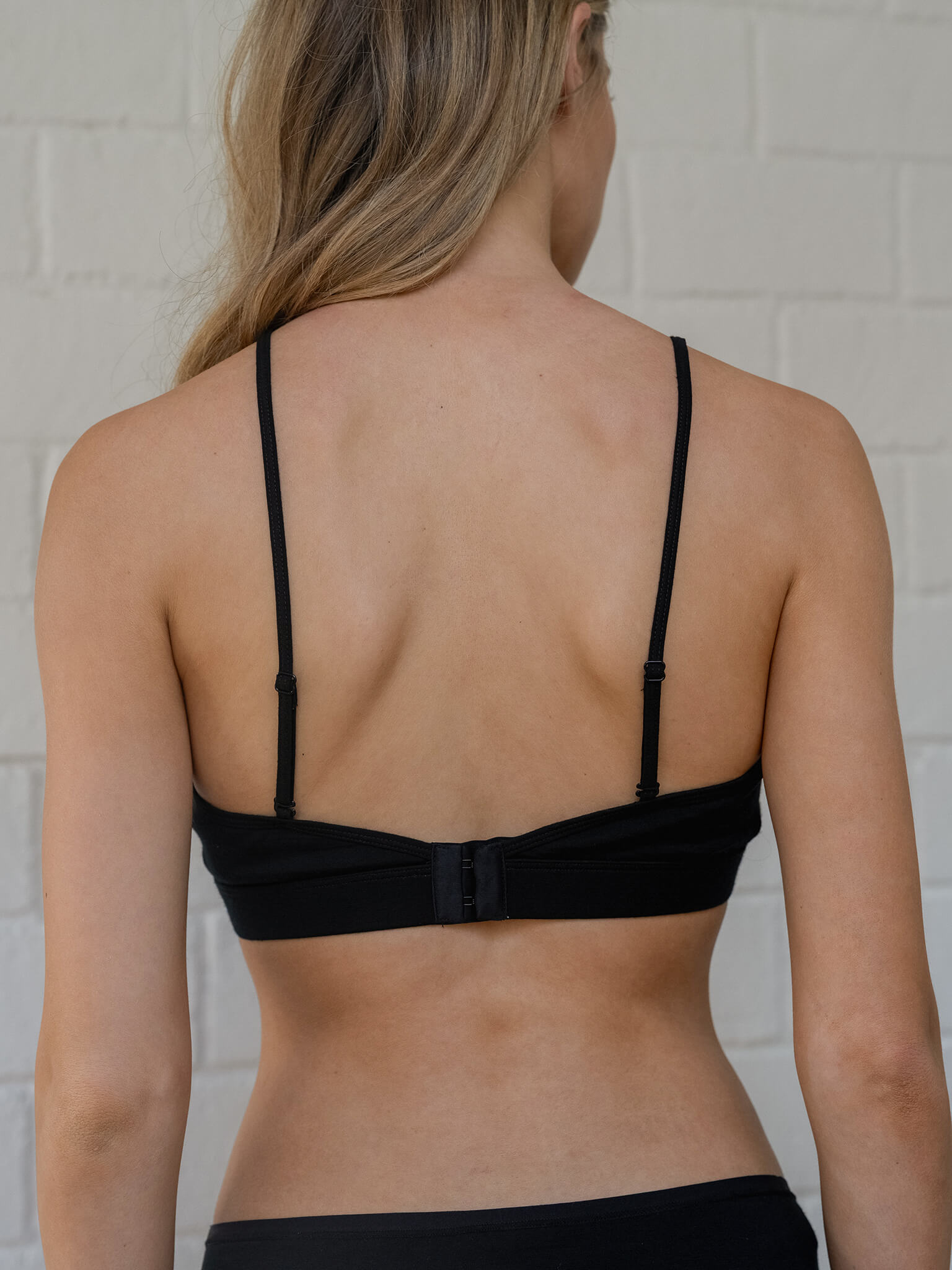 Person wearing a black bra against a white brick wall