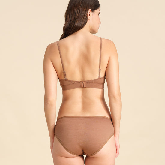Back view of woman wearing a cinnamon Merino wool triangle bra and underwear set against the background.