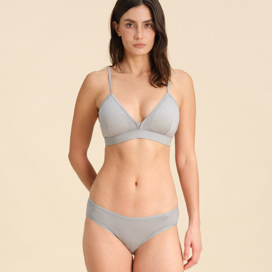 Woman wearing a grey Merino wool triangle bra and underwear set against the background.