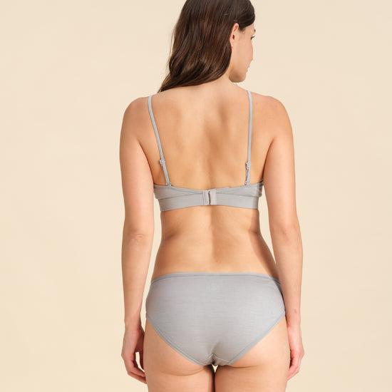 Back view of woman wearing a grey Merino wool triangle bra and underwear set against the background.