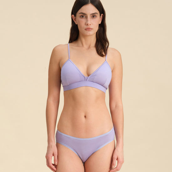 Woman wearing a lavender Merino wool triangle bra and underwear set against the background.