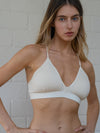 Woman wearing a beige bikini top against a white brick wall.