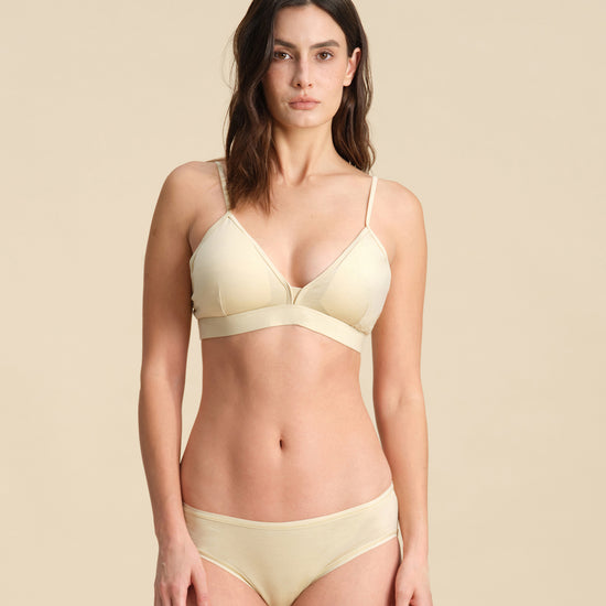 Woman wearing a sand Merino wool triangle bra and underwear set against the background.
