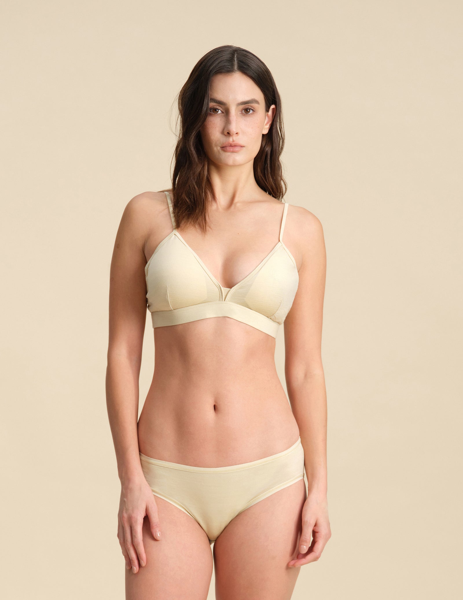 Woman wearing a sand Merino wool triangle bra and underwear set against the background.
