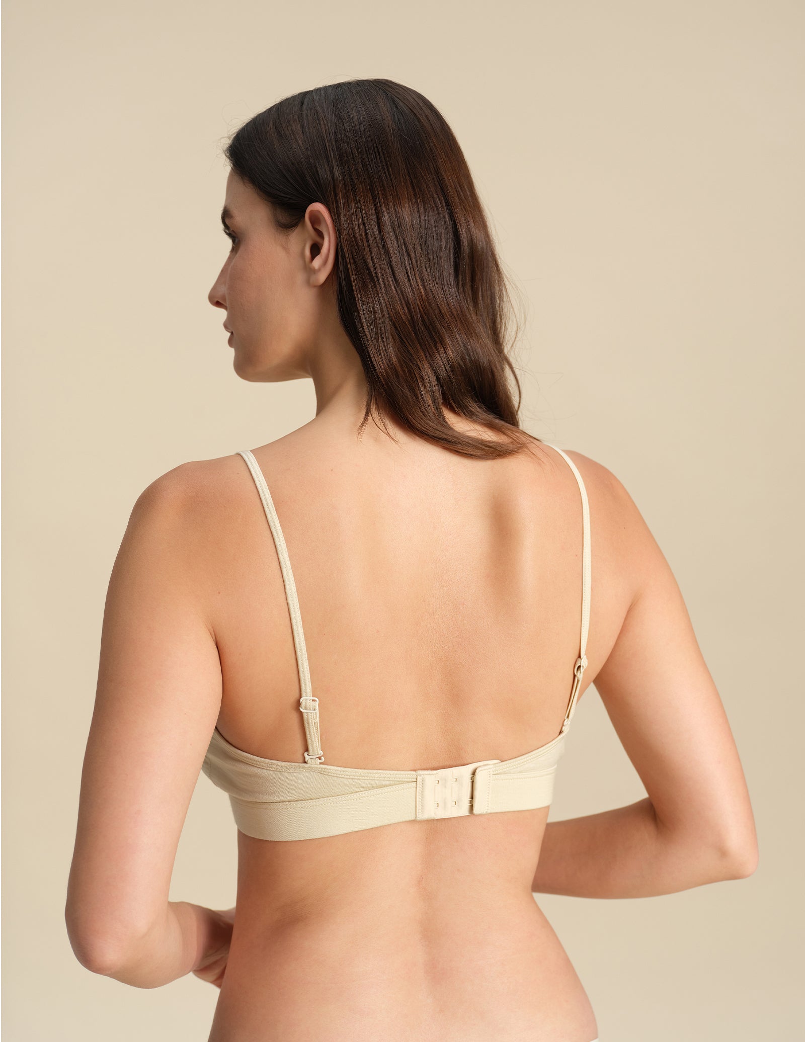 Back view of Woman wearing a sand Merino wool triangle bra against the background