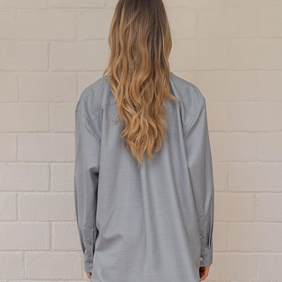 Person wearing a light gray long-sleeve shirt against a beige tiled wall.